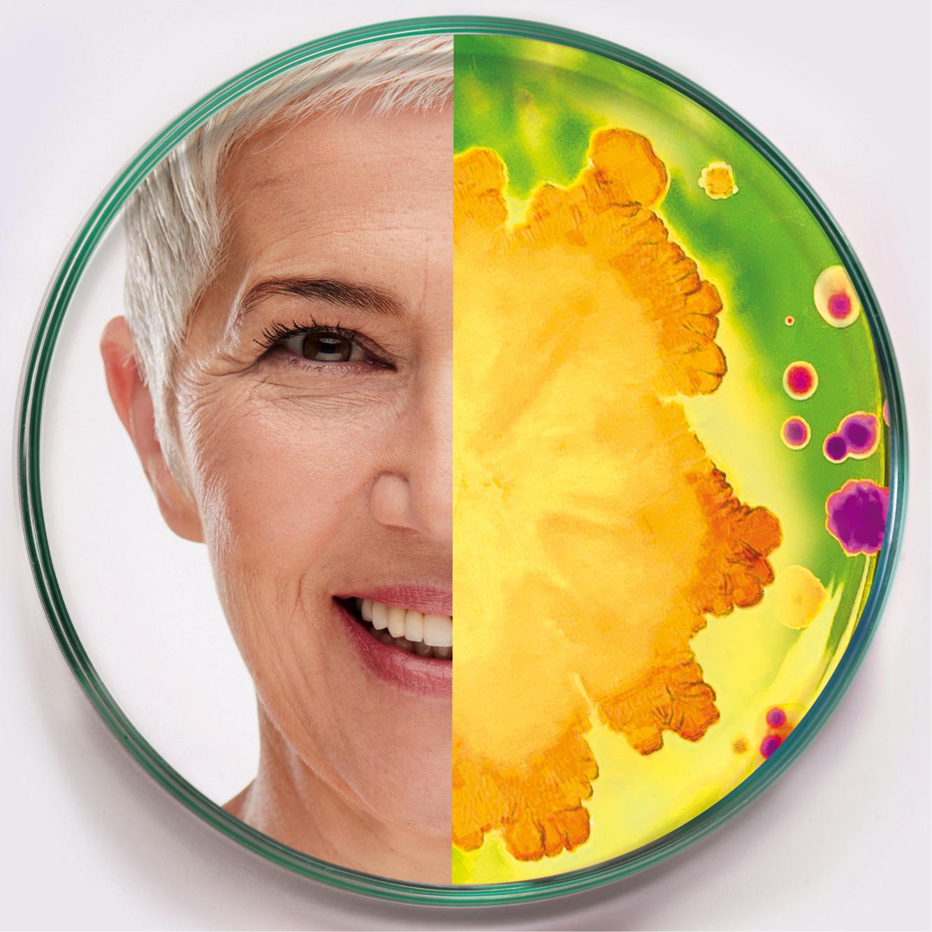 An image split in half shows the left side of an older woman's smiling face on a white background and the right side of a colorful, abstract pattern resembling a microscopic view of bacteria in a petri dish, with hues of green, yellow, orange, and purple.