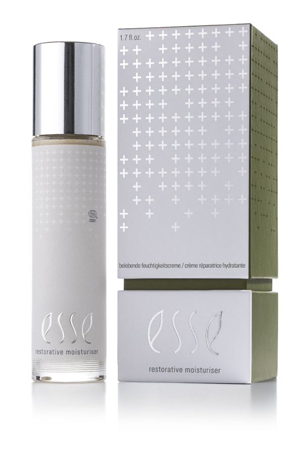 A bottle and box of Esse Restorative Moisturiser. The bottle has a silver cap, clear container, and white-silver accents. The green and silver box features white plus signs and product details.