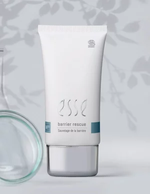 A white tube labelled “Import placeholder for 57617” stands upright with a silver cap. The background features a soft, leafy shadow and blurred glass objects.